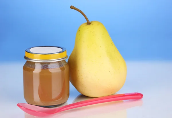 Comida para bebés útil y sabrosa con pera y cuchara sobre fondo azul — Foto de Stock