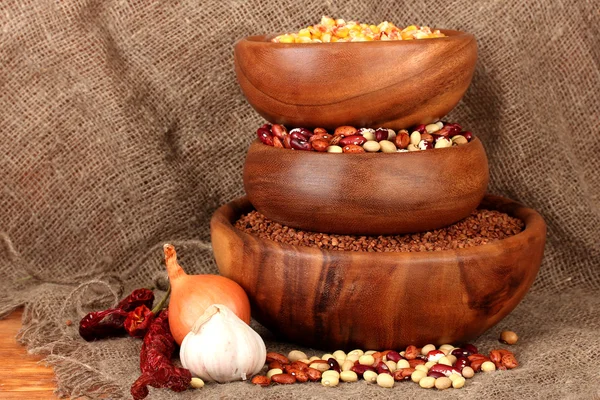 Milho cru, trigo sarraceno e feijão em tigelas de madeira na mesa sobre fundo de pano de saco — Fotografia de Stock