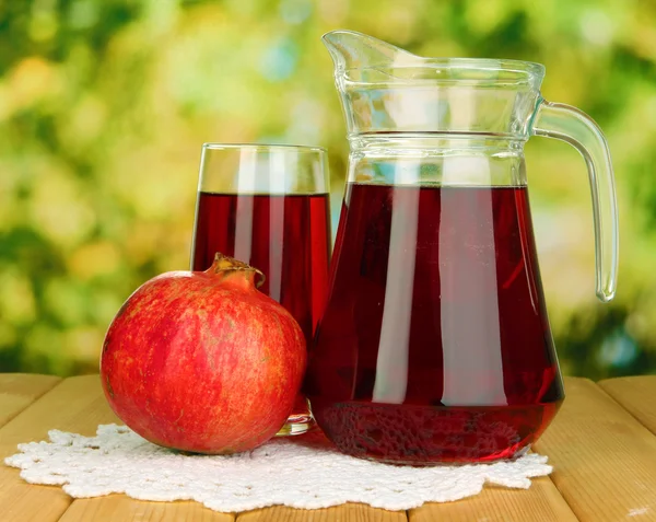 Full glass and jug of pomegranate juice and pomegranate on wooden table outdoor — Stock Photo, Image