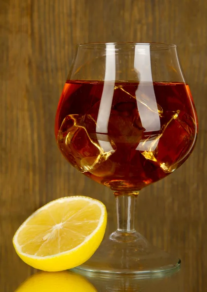 Vaso de brandy con hielo y limón sobre fondo de madera — Foto de Stock