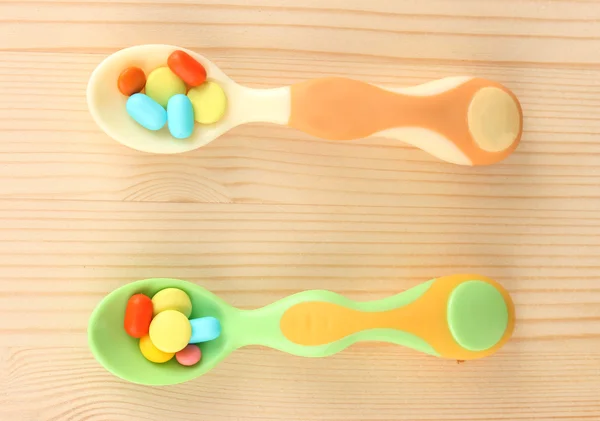 Cucchiai di plastica con pillole di colore su sfondo di legno — Foto Stock