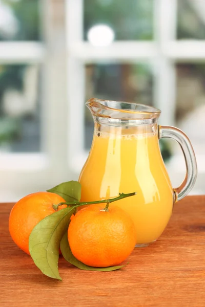 Jarra llena de jugo de mandarina, sobre mesa de madera sobre fondo brillante —  Fotos de Stock