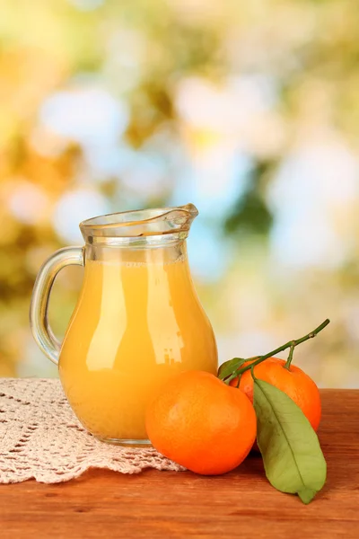 Pełny dzbanek soku pomarańczowego, na drewnianym stole na jasnym tle — Zdjęcie stockowe