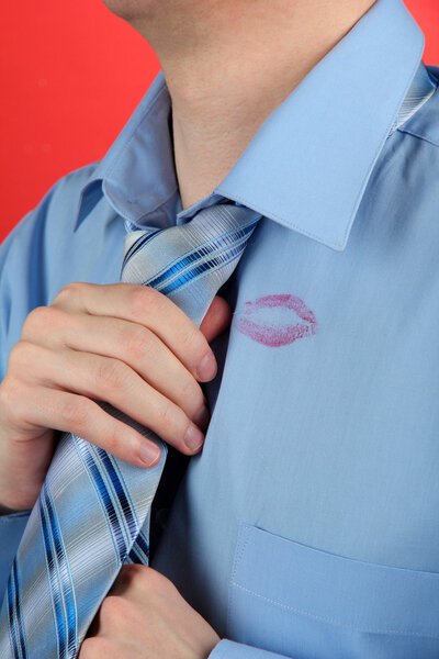 Lipstick kiss on shirt collar of man, on red background