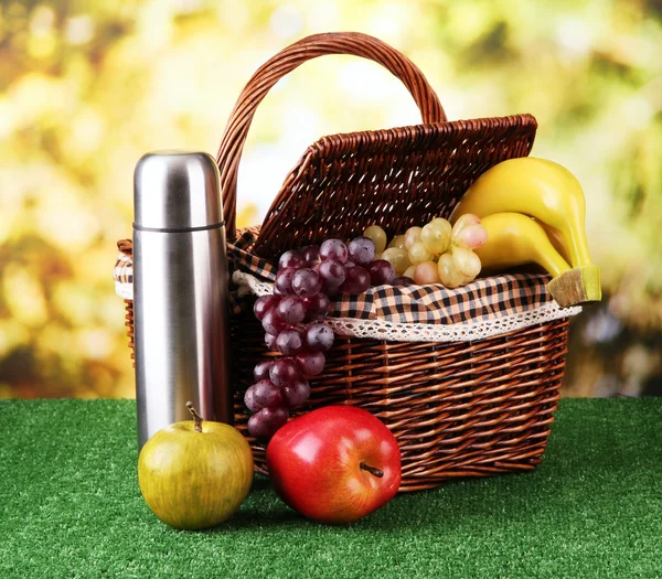 Picnic basket and thermos on grass on bright background — Stock Photo, Image