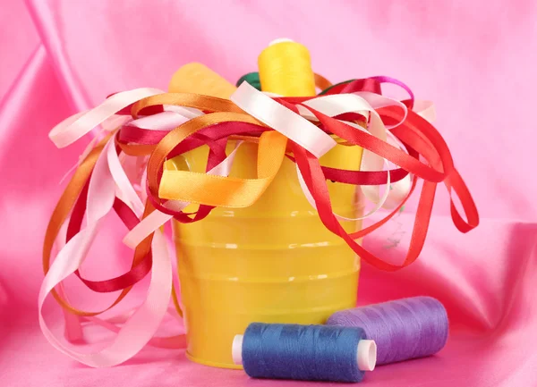 Color bucket with multicolor ribbons and thread on pink fabric background — Stock Photo, Image