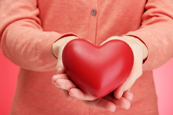 Κόκκινη καρδιά στα χέρια γυναίκα, σε κόκκινο φόντο — Φωτογραφία Αρχείου