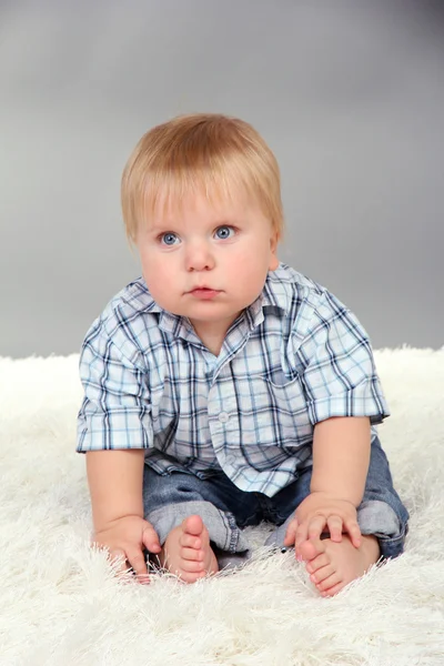 Niño sentado en alfombra blanca sobre fondo gris —  Fotos de Stock