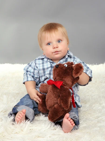 Niño sentado en alfombra blanca sobre fondo gris —  Fotos de Stock