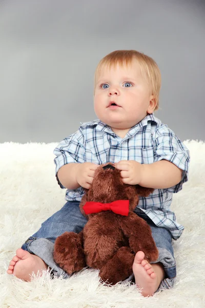 Liten pojke sitter på vita mattan på grå bakgrund — Stockfoto