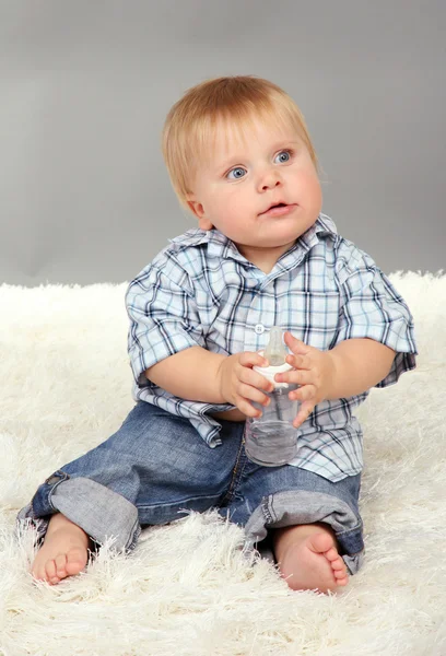 Petit garçon assis sur un tapis blanc sur fond gris — Photo