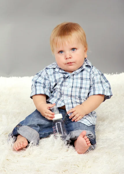 Liten pojke sitter på vita mattan på grå bakgrund — Stockfoto