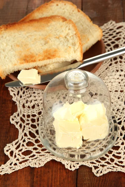 Масло на стеклянном блюдце со стеклянным покрытием и свежим хлебом, на деревянном фоне — стоковое фото
