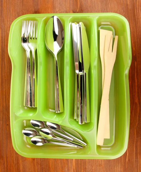 Green plastic cutlery tray with checked cutlery on wooden table — Stock Photo, Image