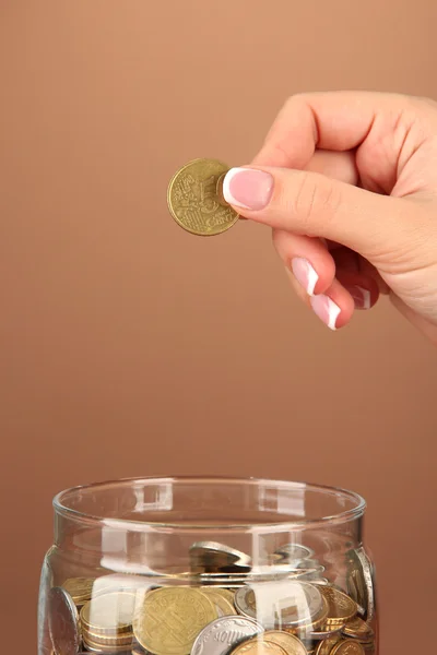 Sparen, weibliche Hand steckt eine Münze in Glasflasche, auf farbigem Hintergrund — Stockfoto