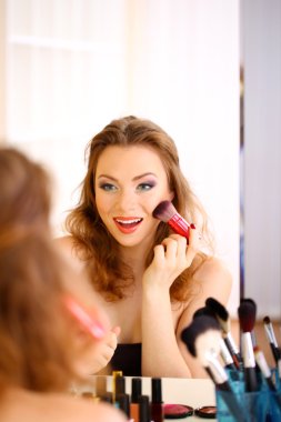 Genç ve güzel bir kadın aynanın yanında makyaj yapıyor.