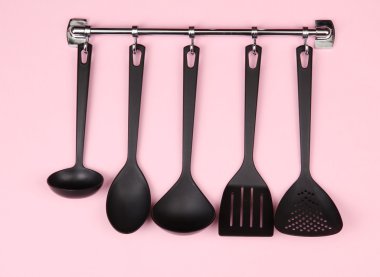 Gümüş kanca, pembe bir arka plan üzerinde siyah mutfak gereçleri