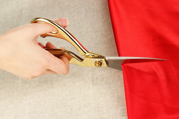 Seamstress corte tecido vermelho no fundo tecido bege — Fotografia de Stock