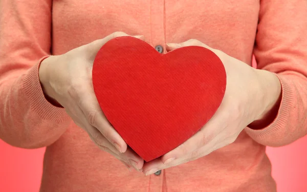 Corazón rojo en manos de mujer, sobre fondo rojo — Foto de Stock