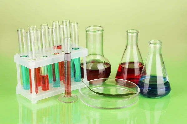 Test-tubes and green leaf tested in petri dish, on color background — Stock Photo, Image