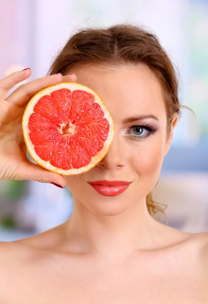 Beautiful young woman with bright make-up, holding grapefruit, on bright background — Stock Photo, Image