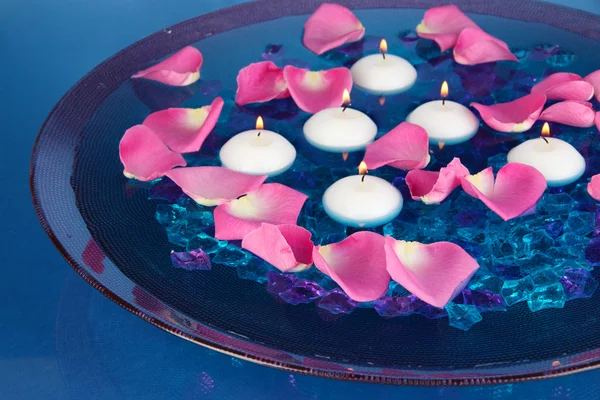 Pétalos de rosa y velas en agua en jarrón sobre fondo azul — Foto de Stock