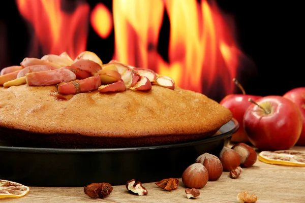 Tasty homemade pie with apples and nuts, on wooden table on flame background — Stock Photo, Image