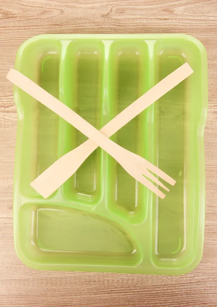 Green plastic cutlery tray with crossed wooden fork and scapula on wooden table — Stock Photo, Image