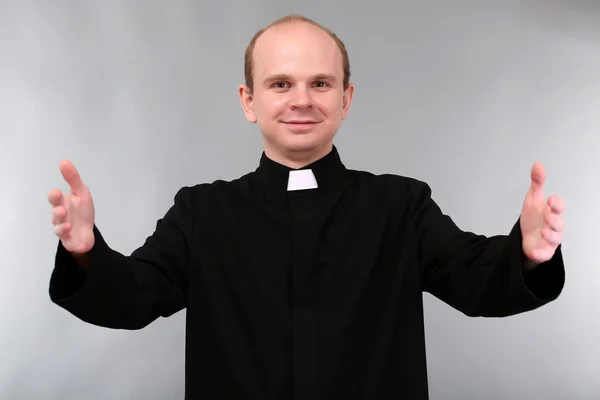 Joven sacerdote sobre fondo gris — Foto de Stock