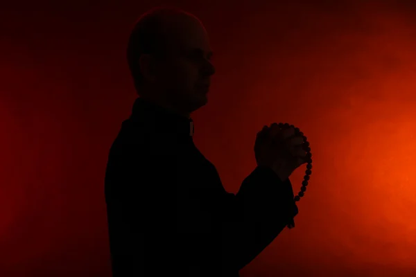 Jovem pastor com rosário de madeira, no fundo vermelho escuro — Fotografia de Stock