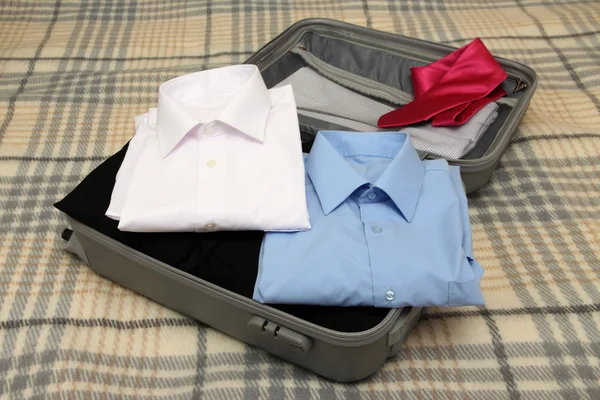 Open grey suitcase with clothing on plaid — Stock Photo, Image