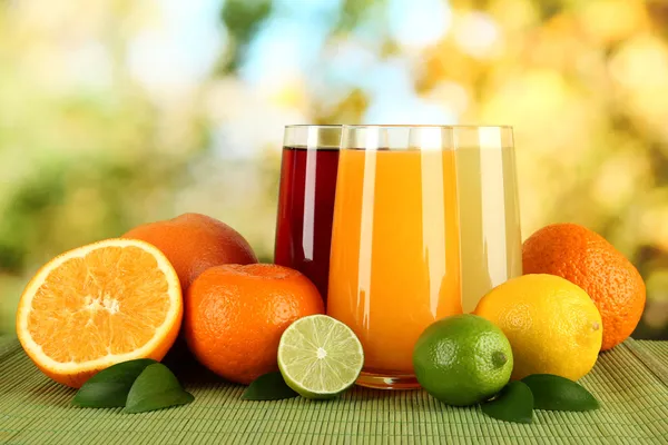 Glasses of juise with leafs and fruits on table on bright background