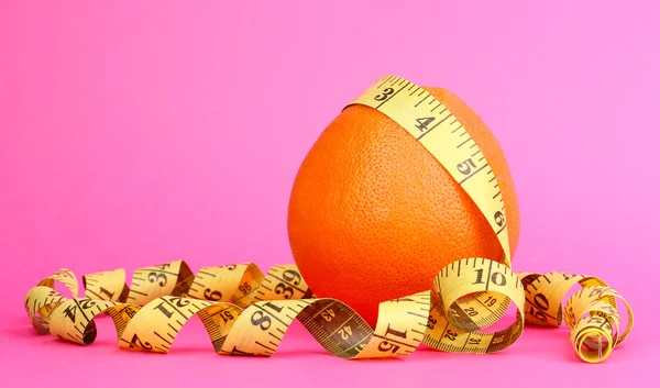Naranja con cinta métrica sobre fondo rosa —  Fotos de Stock