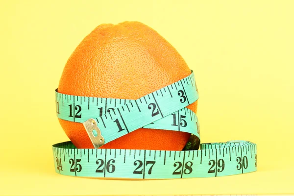 Orange with measuring tape on yellow background — Stock Photo, Image