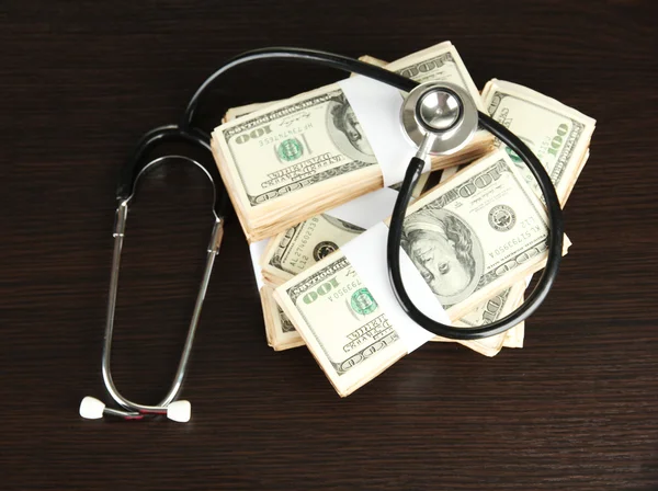 Healthcare cost concept: stethoscope and dollars on wooden background — Stock Photo, Image