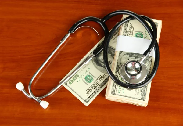 Conceito de custo de cuidados de saúde: estetoscópio e dólares em fundo de madeira — Fotografia de Stock