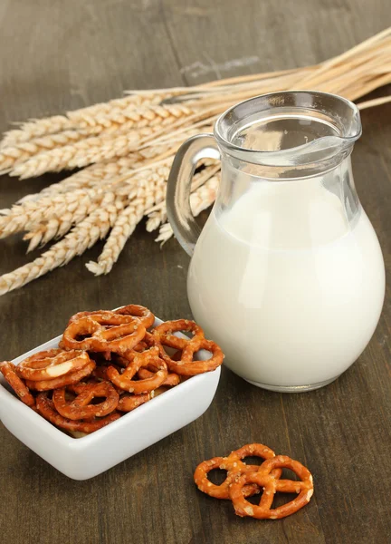 Sabrosos pretzels en tazón blanco y jarra de leche en la mesa de madera de cerca — Foto de Stock