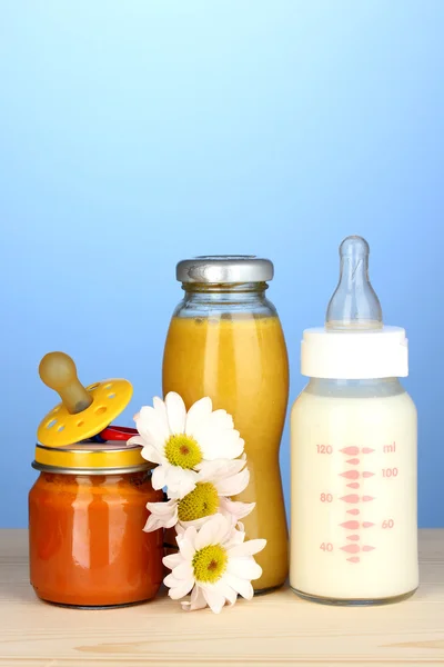 Żywność dla niemowląt, butelki mleka, przeciery i soki na niebieskim tle — Zdjęcie stockowe
