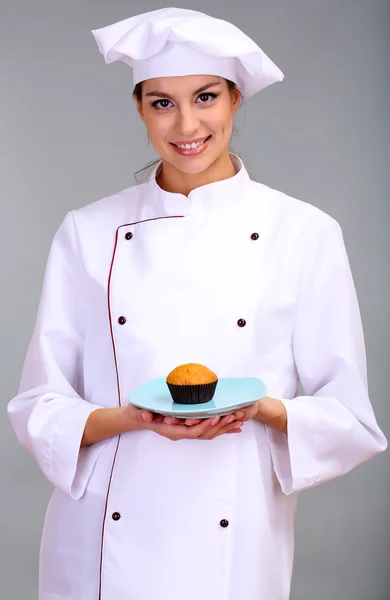 Retrato de jovem chef com bolo em fundo cinza — Fotografia de Stock