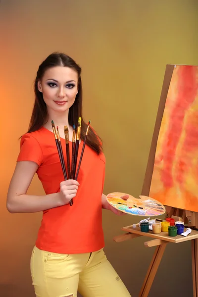 Beautiful young woman painter at work, on bright color background — Stock Photo, Image