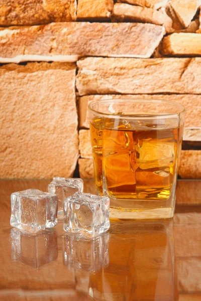Стакан виски и лед на фоне кирпичной стены — стоковое фото