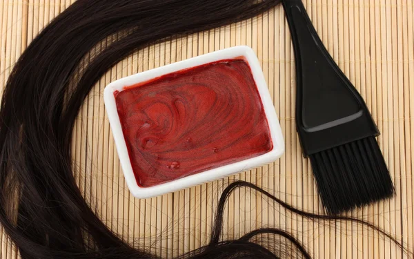 Hair dye in bowl and brush for hair coloring on beige bamboo mat, close-up Royalty Free Stock Images