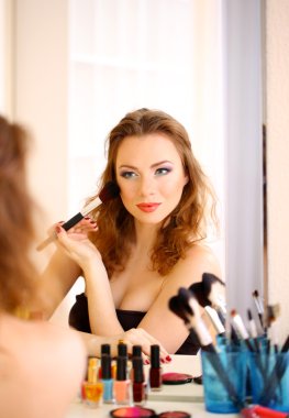 Genç ve güzel bir kadın aynanın yanında makyaj yapıyor.