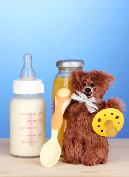 Baby bottle of milk, juice and teddy bear on blue background — Stock Photo, Image