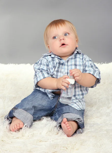 Liten pojke sitter på vita mattan på grå bakgrund — Stockfoto