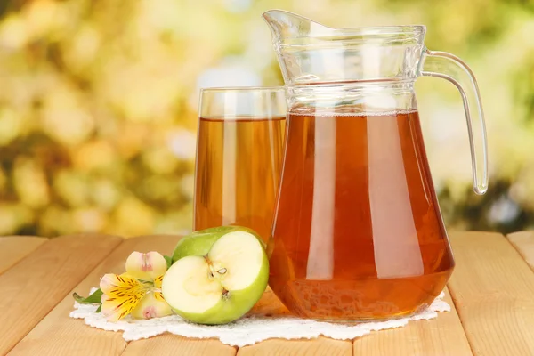 Vol glas en kruik van appelsap en appels op houten tafel buiten — Stockfoto