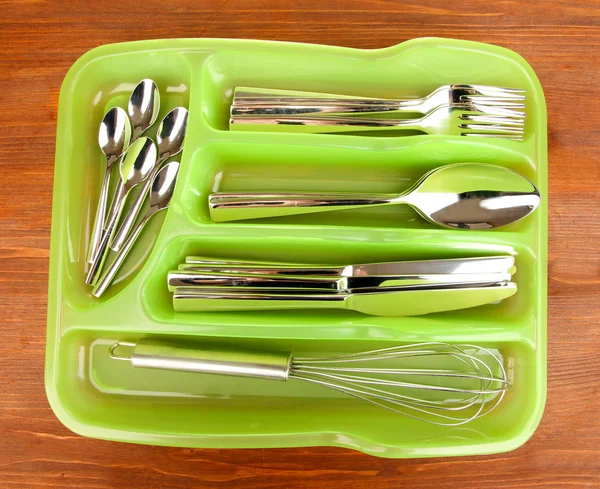 Green plastic cutlery tray with checked cutlery on wooden table — Stock Photo, Image