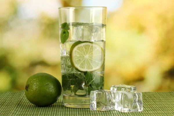 Bicchiere d'acqua con ghiaccio, menta e calce sul tavolo su sfondo luminoso — Foto Stock