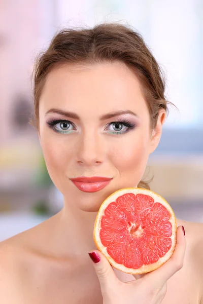 Bella giovane donna con trucco luminoso, tenendo il pompelmo, su sfondo luminoso — Foto Stock