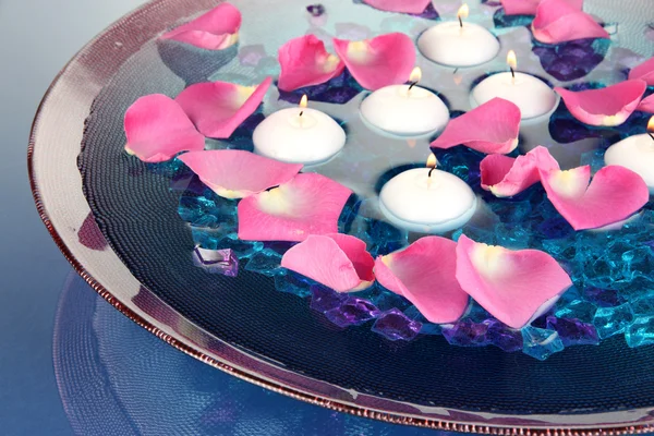 Petali di rosa e candele in acqua in vaso su sfondo blu primo piano — Foto Stock